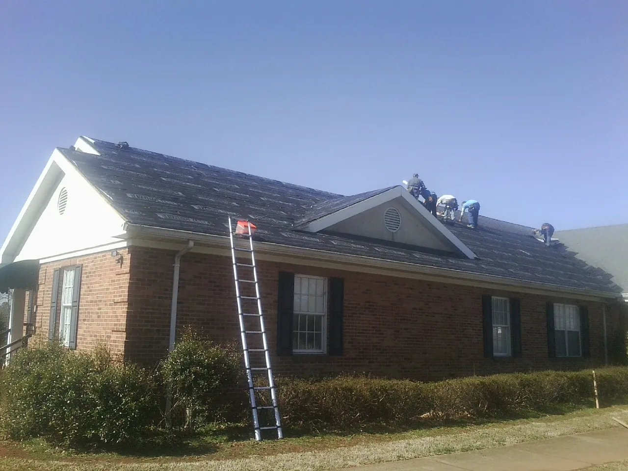 Crew tearing shingles off a brick ranch roof with a ladder set — Metal Roof Repair work by our crew in Sheffield Lake