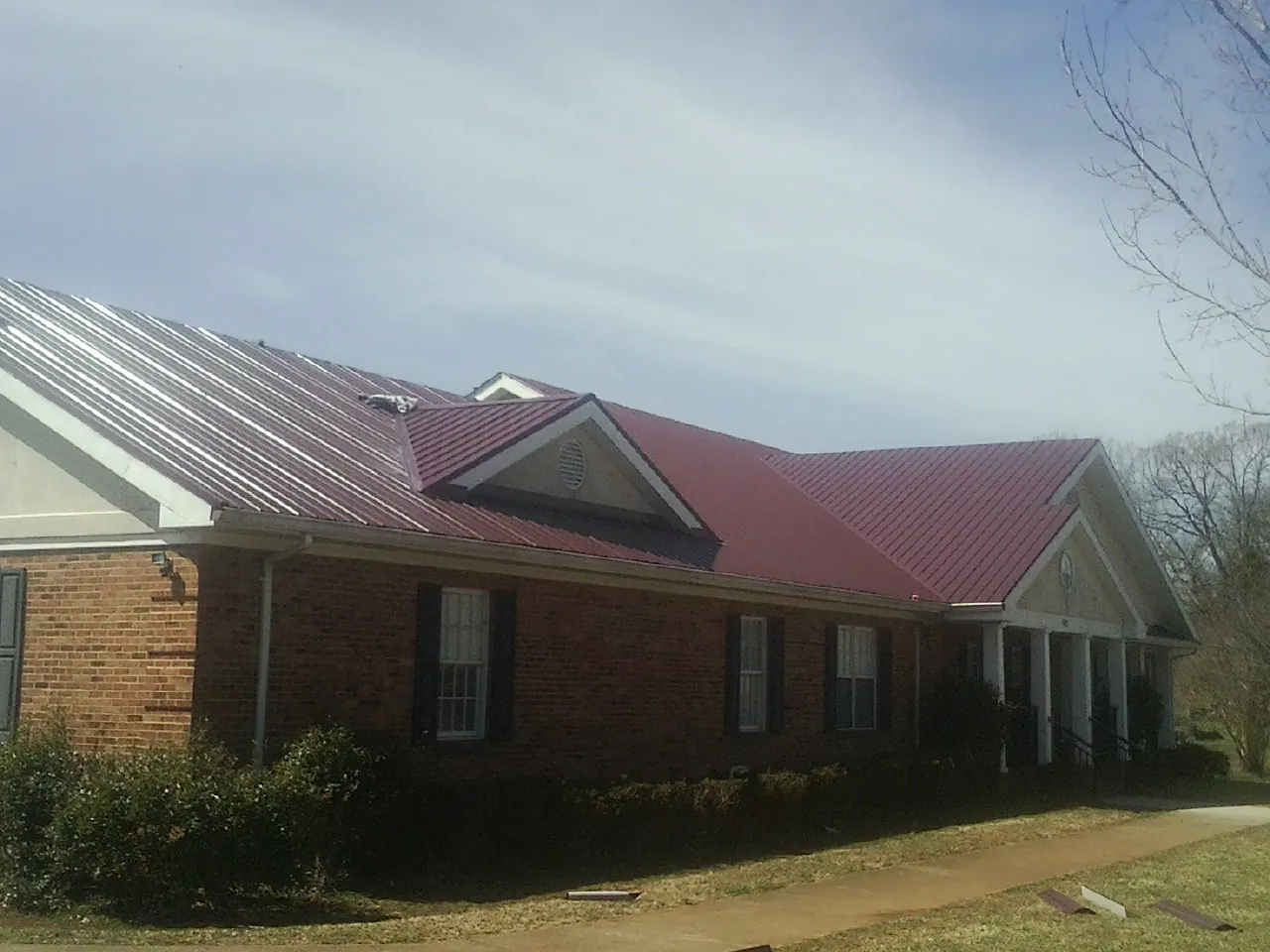 Red metal roof with gabled entries on a long brick building, from a Hail Damage Roof Repair job in Sheffield Lake