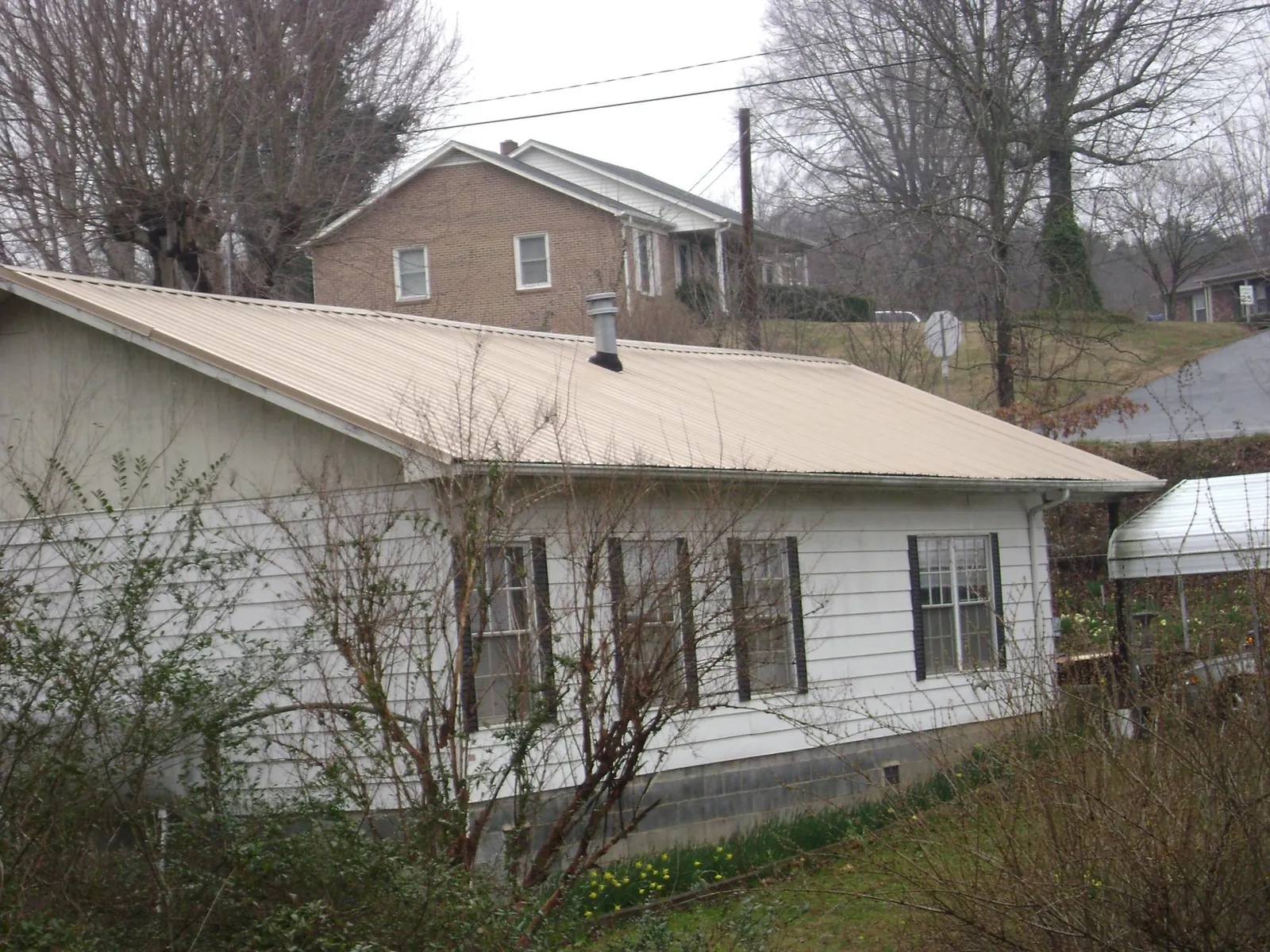 Tan metal roof on a white sided house set into a hillside — Commercial Roofing by Roofing Brothers in Sheffield Lake