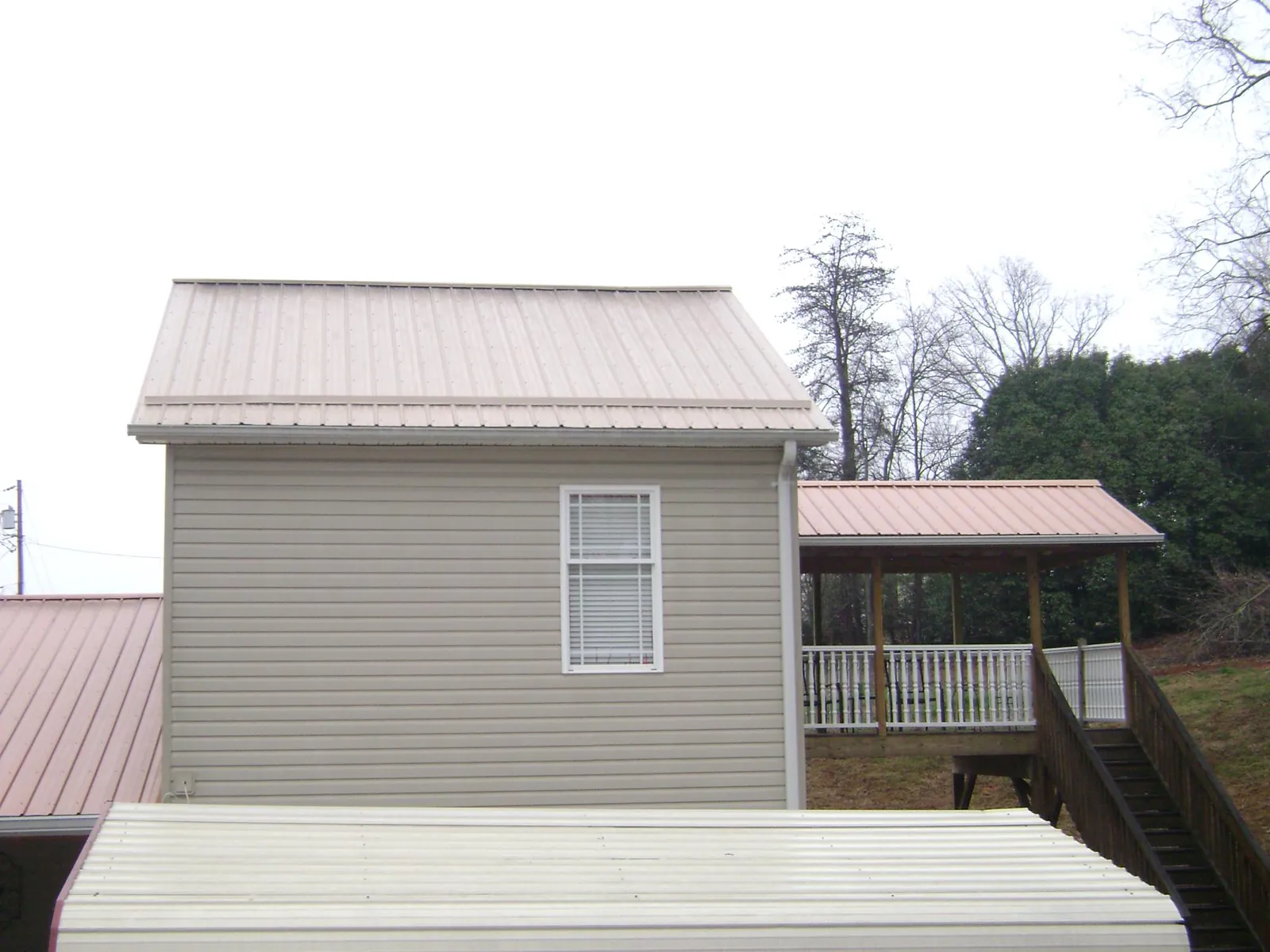 Tan metal roofs on a two story addition and attached porch, from a Roof Replacement job in Sheffield Lake